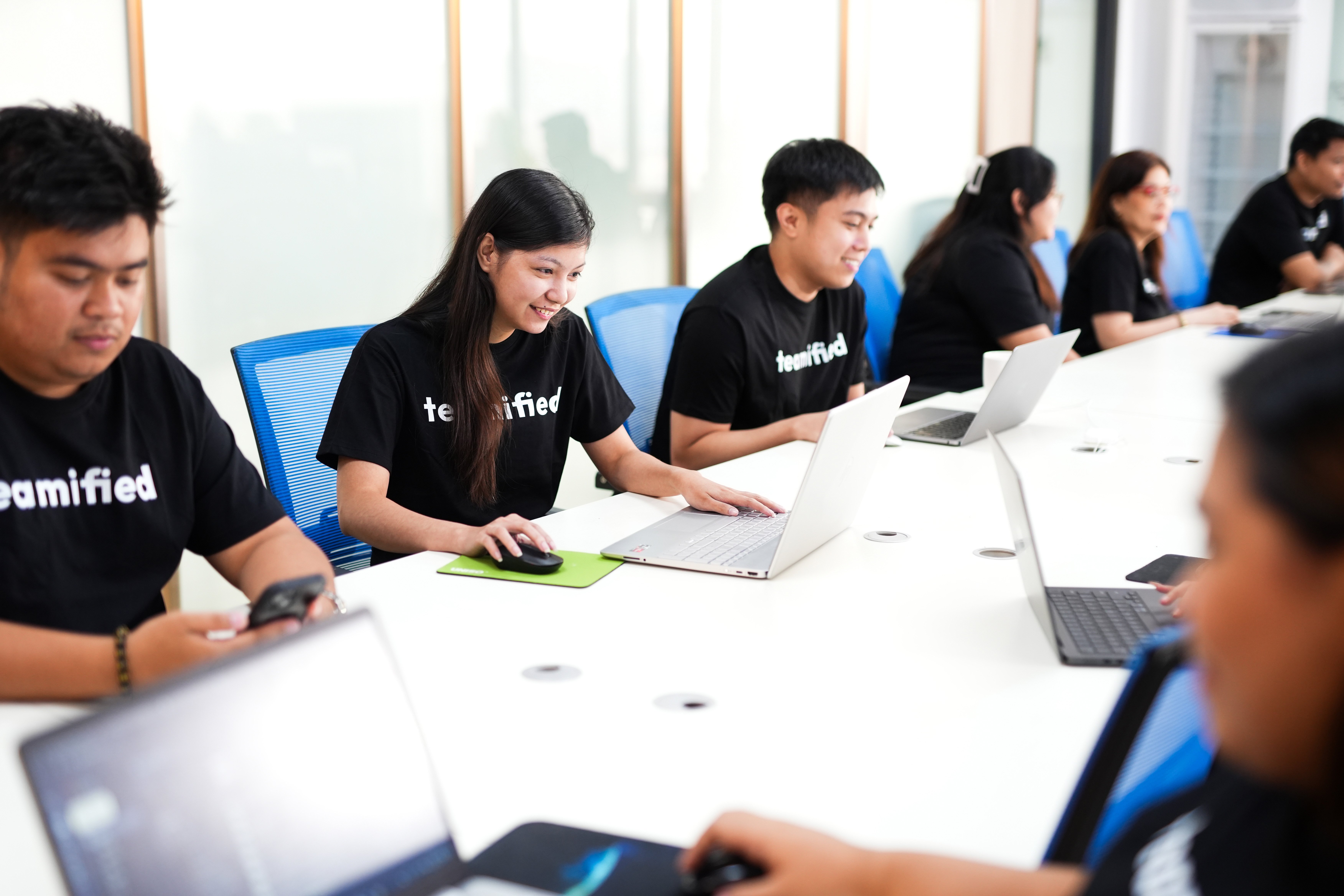Teamified team members working on laptops in a collaborative office environment during a team meeting.
