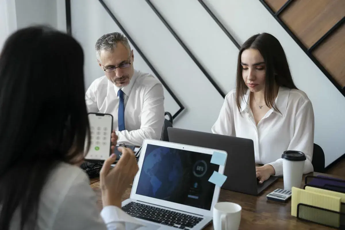 Business team discussing data on laptops during a meeting, with one person showing a smartphone screen