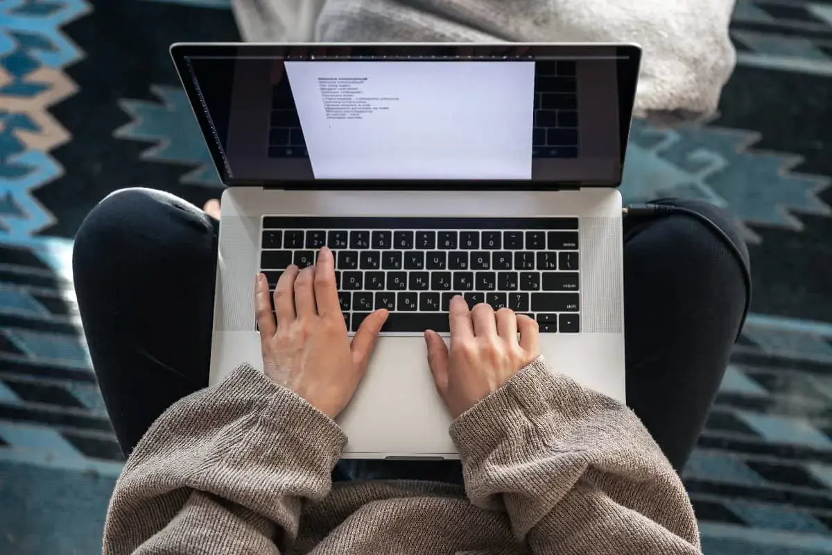 Woman typing on a laptop while sitting cross-legged, viewed from above.
